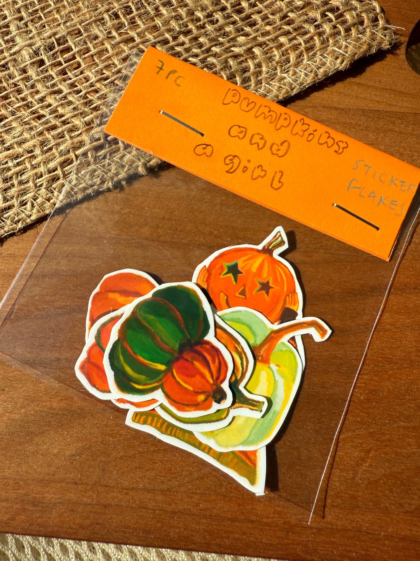 A clear plastic bag containing colorful autumn-themed stickers shaped like pumpkins and gourds, with an orange handwritten label reading 'pumpkins and a girl' on a wooden surface.